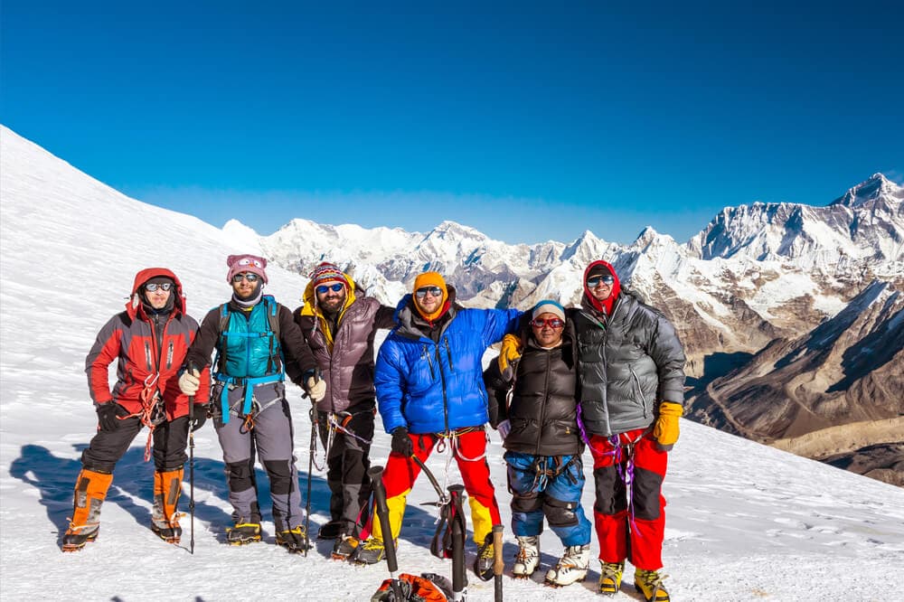 A group of high altitude hikers on top of snow capped moutain with blue skies in assorted down jackets