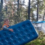 Camper carries blue air mattress fully pumped to tent out in the wilderness