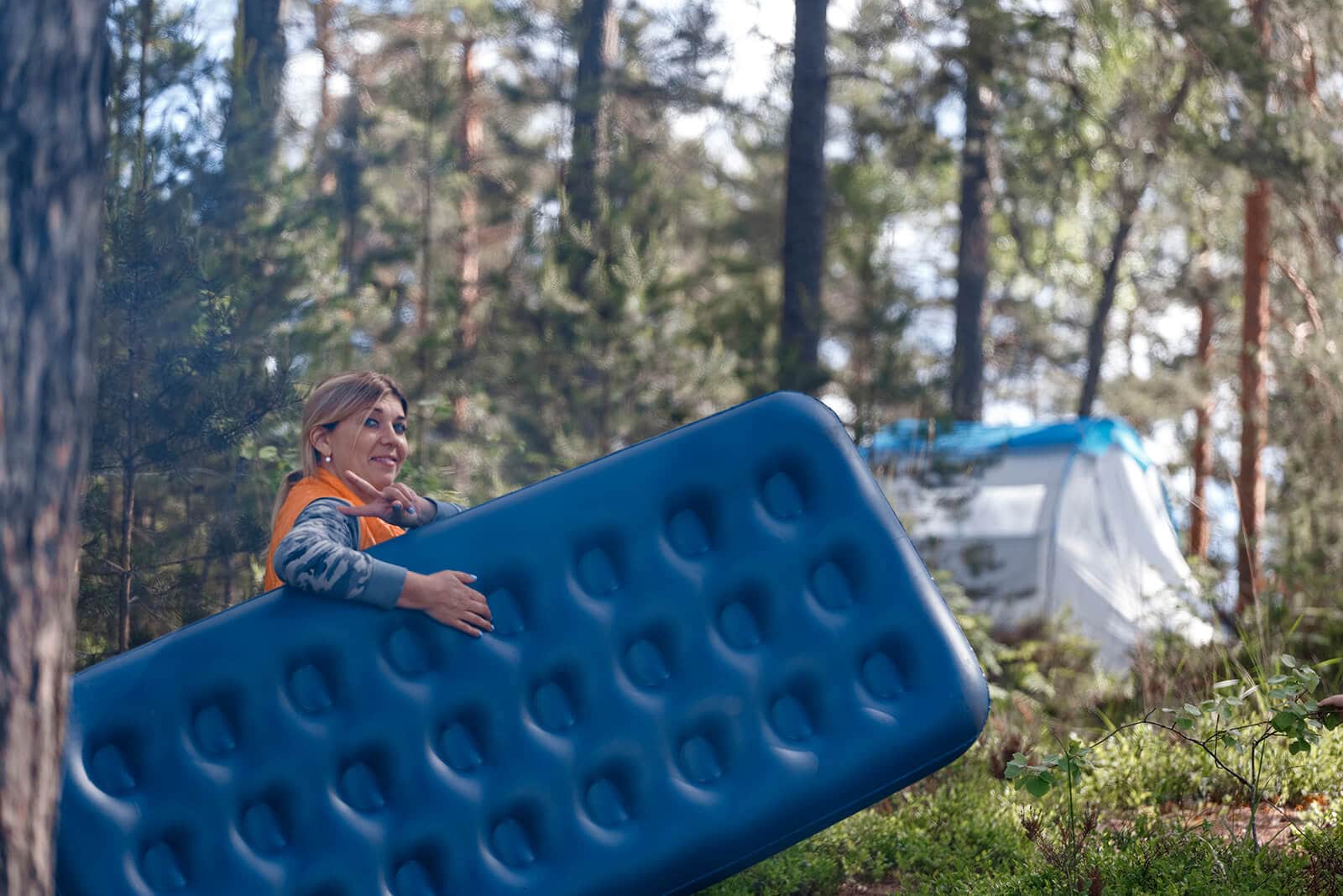 Camper carries blue air mattress fully pumped to tent out in the wilderness