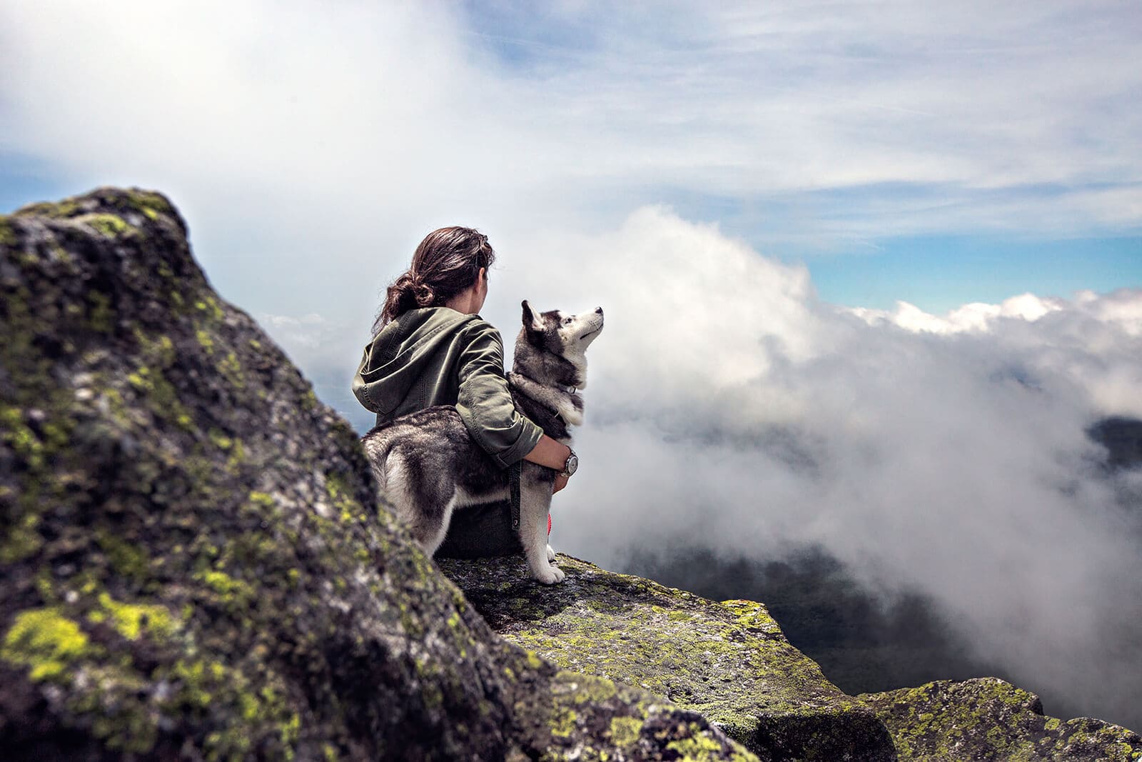 Female hiker and husky dog taking a rest on lookout during hike