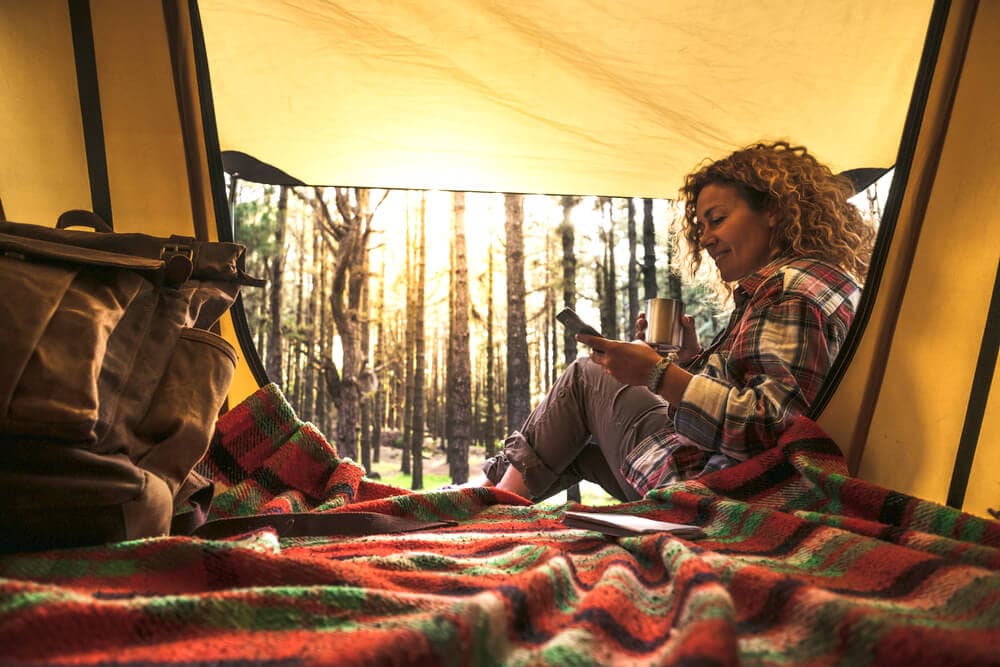 Female camper enjoying early morning light in dark blackout tent