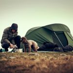 Hiker and canine companion getting tent warm and ready in winter camping location