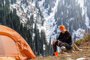 Lone camper prepping morning instant coffee while camping snow capped mountains