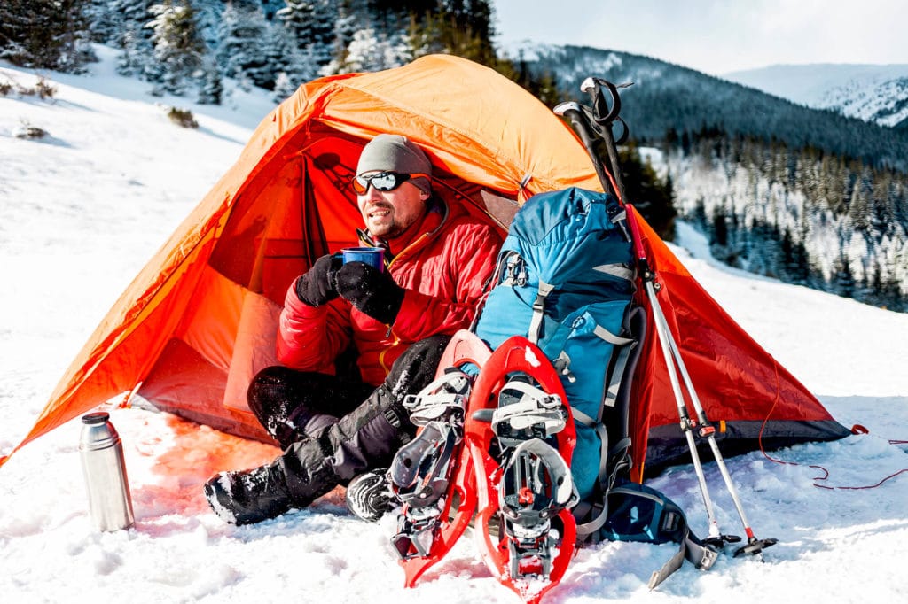 Male camper sitting in hot warm tent in snow morning light ready for adventure