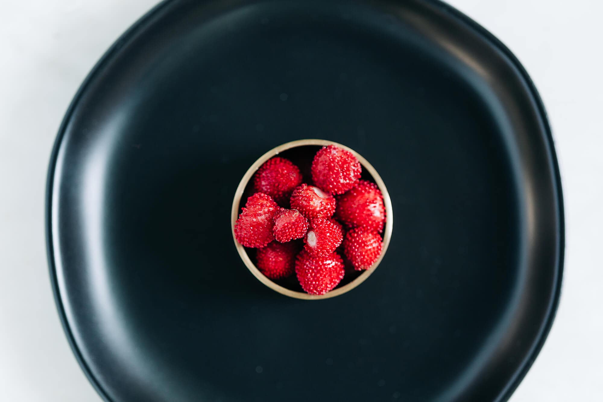 Plating of snake berries inidan mockberry in cup on black plate