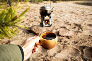 Small woodburning stove with hot cup of coffee while camping