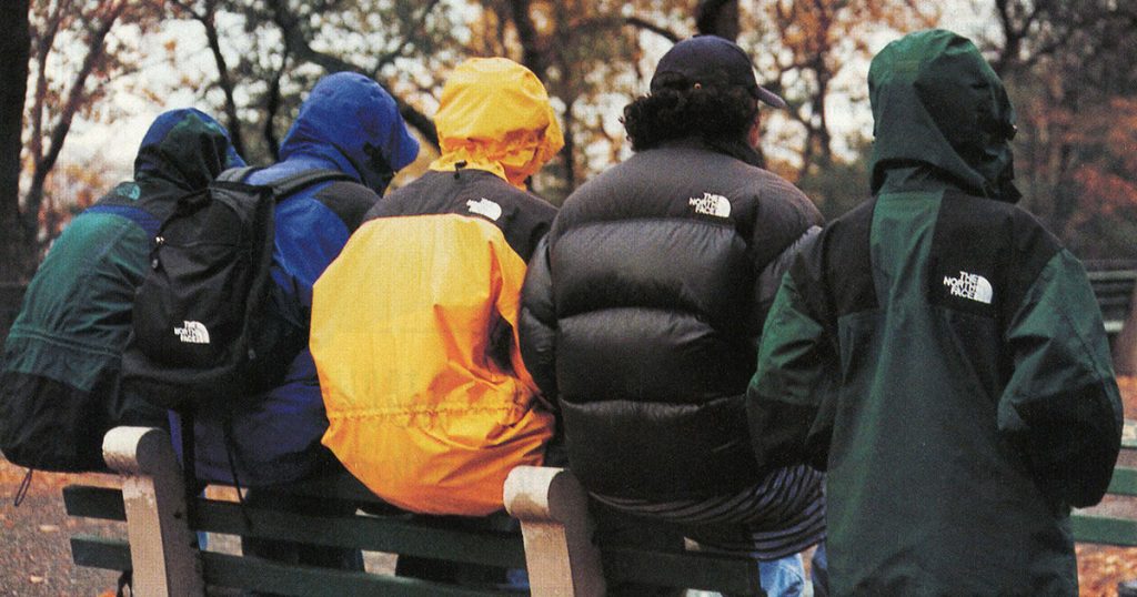 Vintage the north face puffer jackets in different colours on people sitting at park bench.